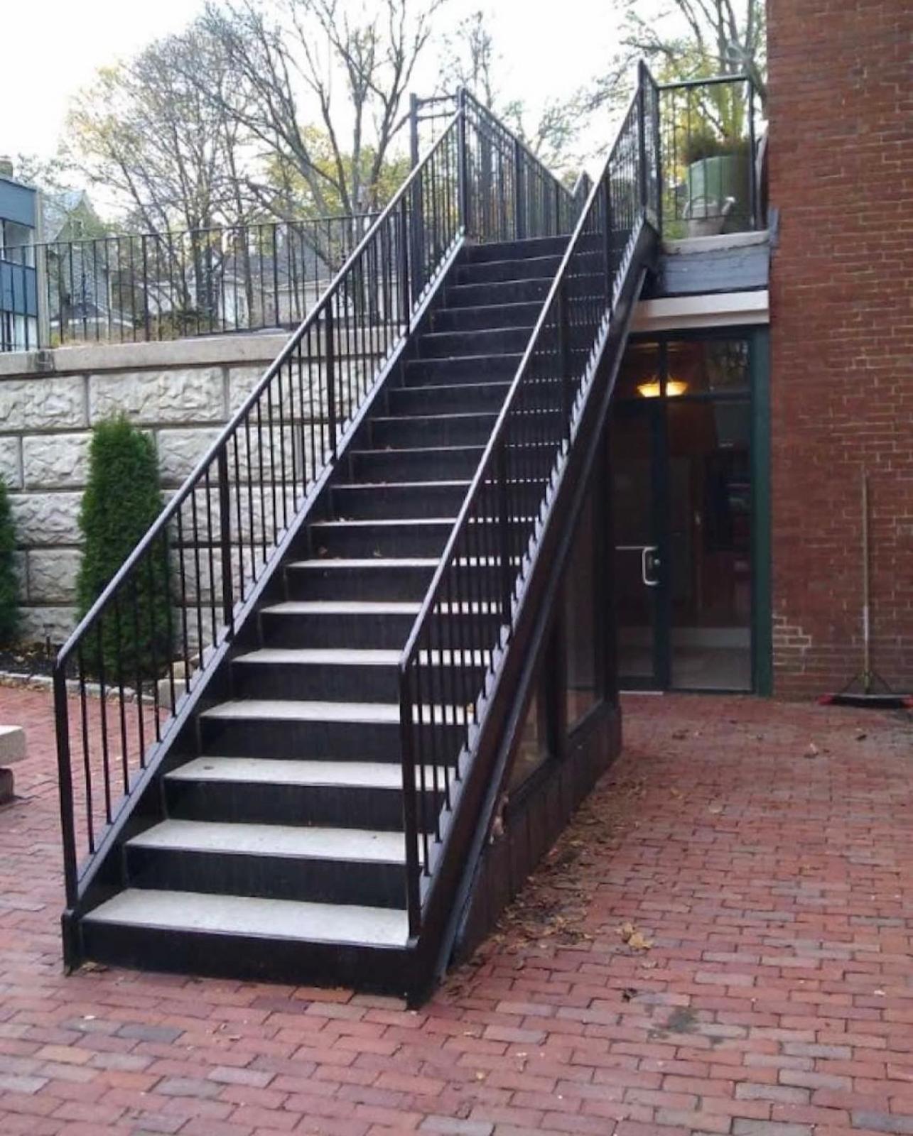 Black steel egress stair with vertical picket railing on a brick building