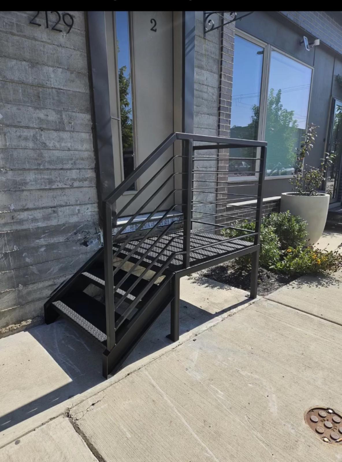Compact black steel entry stair with horizontal railing at a storefront