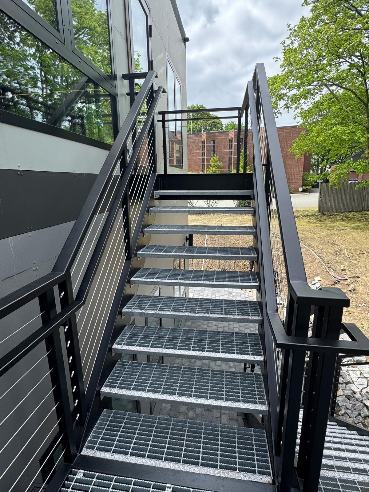 Steel stair with grating treads and cable railing beside large windows